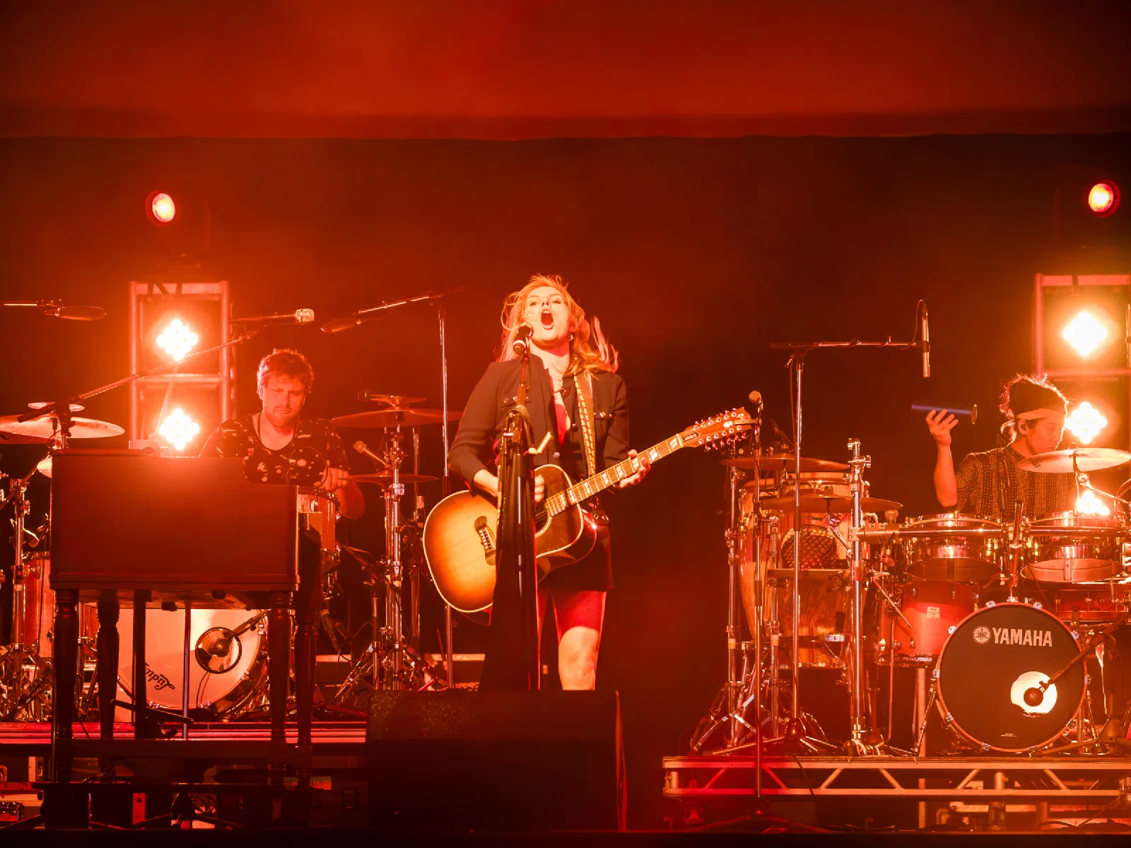 Grace Potter singing and playing guitar under red stage lights