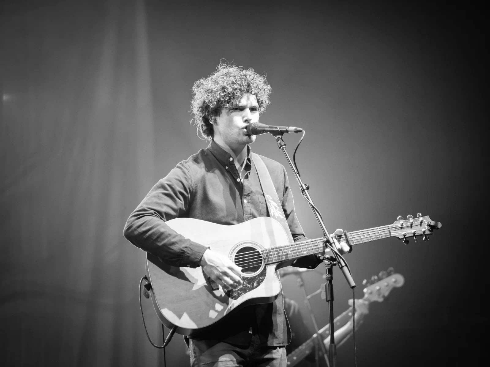 Black and white portrait of Vance Joy singing and playing acoustic guitar