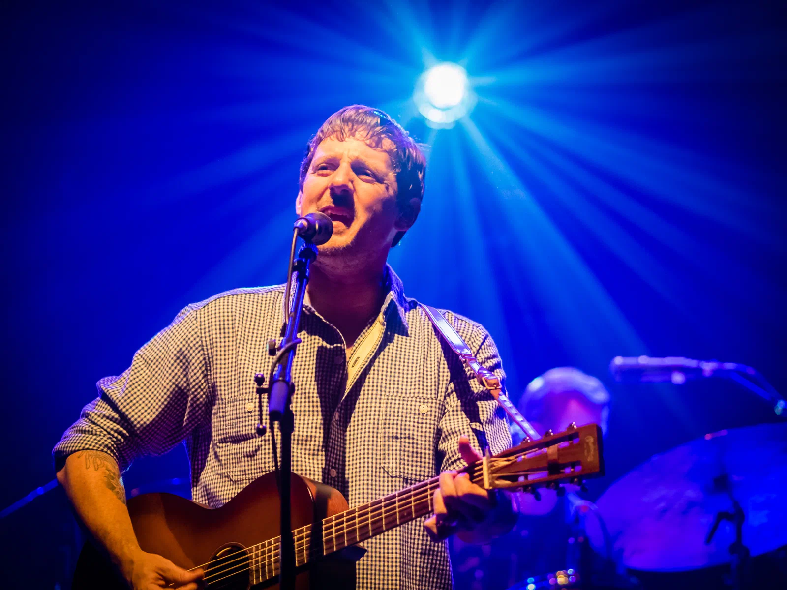 Sturgill Simpson singing and playing acoustic guitar under blue stage lights